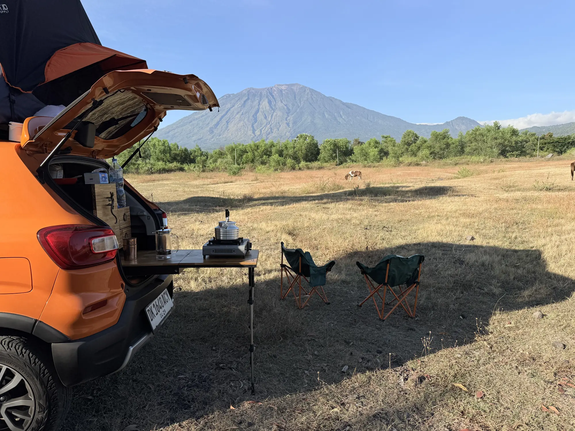 Tailgate kitchen with a coffee set and two camp chairs facing a volcano